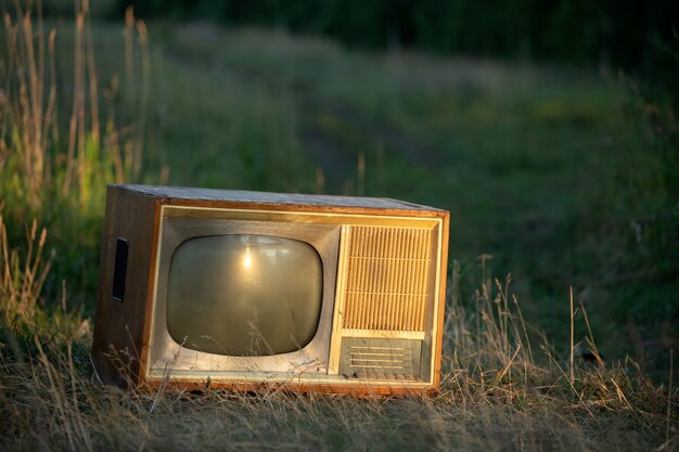 Foto antiga tv retrô em uma estrada de campo contra um fundo de trigo sob os raios do sol poente