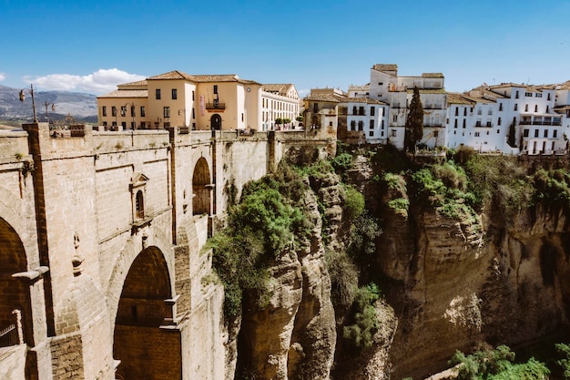 Antiga vila de anadaluzia com ponte alta e casas sobre formação rochosa em dia ensolarado