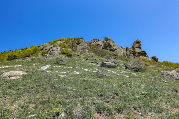 Antigas montanhas de pedra calcária de forma arredondada na neblina do ar. O Vale dos Fantasmas. Demerji. Árvores verdes e arbustos em primeiro plano. Maio de 2021. Crimeia.