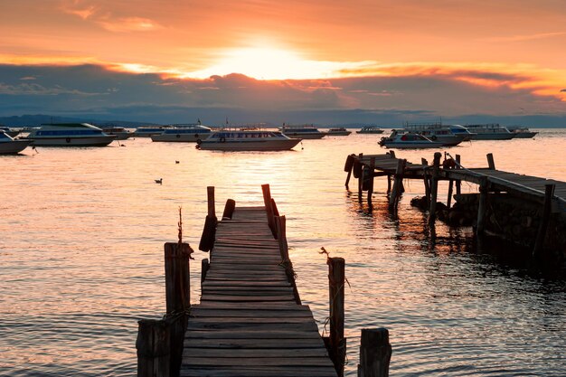 Antigo cais de madeira e barcos na margem do lago Titicaca ao pôr do sol em Copacabana, Bolívia