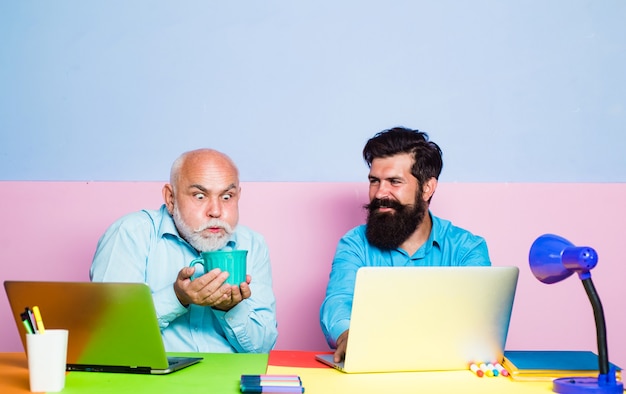 Antigo gerente tendo uma conversa amigável em uma reunião com laptops velhos e jovens empresários usando nota ...