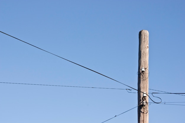 Antigo poste de telefone de madeira decrépito contra um céu azul degradê