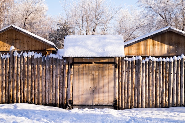 Antigua casa en el bosque siberiano cercada con nieve empalizada.