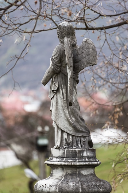 Antigua escultura de lápida de un ángel con el brazo roto y las alas en el cementerio