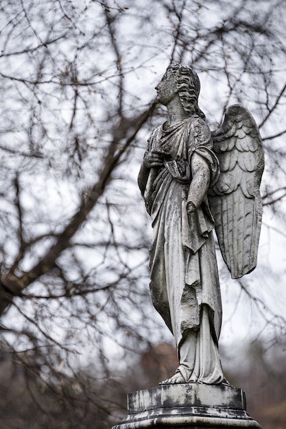 Antigua escultura de lápida de un ángel con el brazo roto y las alas en el cementerio