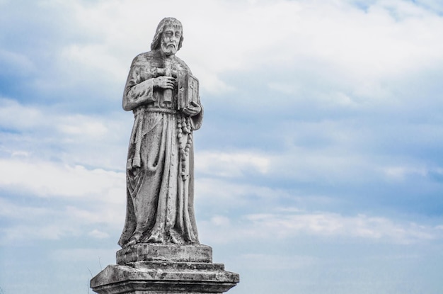 Antigua estatua religiosa en el antiguo cementerio en el cielo de fondo con nubes Jesús con biblia