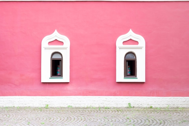 Una antigua fachada rosa con dos ventanas blancas. Geometría arquitectónica.