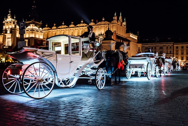 La antigua plaza de la noche cracovia con luminosos carruajes tirados por caballos