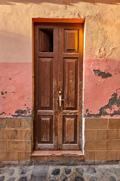 Antigua puerta de madera dañada de un edificio abandonado y desgastado Entrada antigua rota y envejecida a una casa en un pequeño pueblo o abajo en un día soleado Puerta antigua y rústica de casa vacante