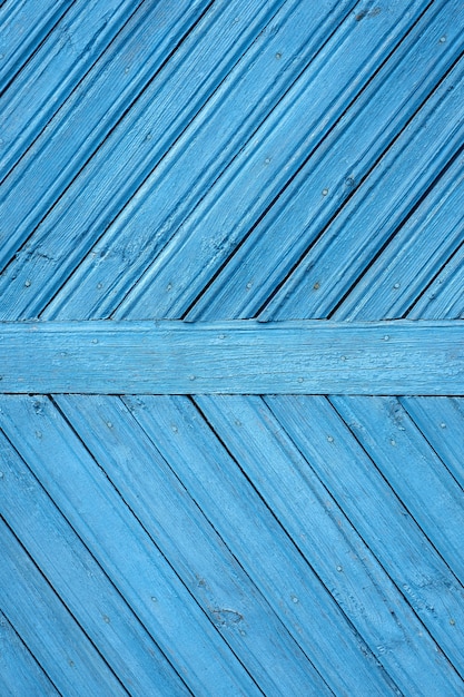 Una antigua puerta de madera con placas azules en la diagonal y pintura descascarada