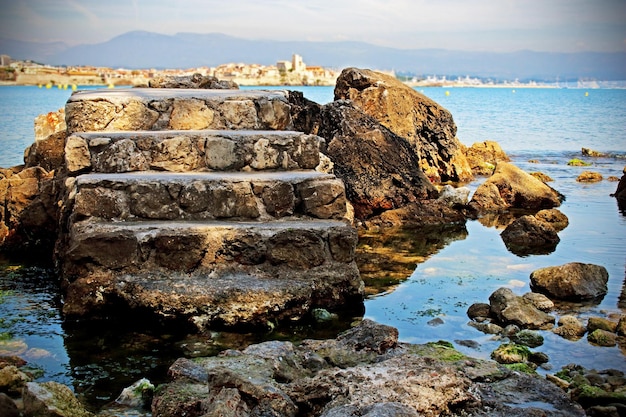 Foto antiguas escaleras de piedra de la torre aisladas en el fondo azul del agua del mar con rocas y montañas en el horizonte