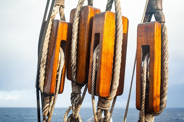 Antiguas poleas de madera de un velero con cuerdas atadas contra el fondo del cielo y el mar