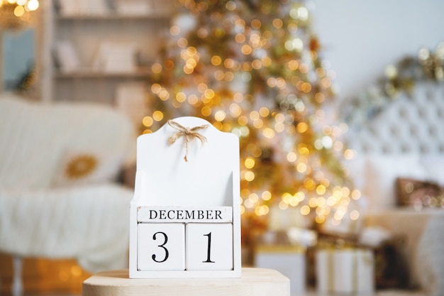 Antiguo calendario vintage de cubos de madera con la fecha del 31 de diciembre en el fondo de un árbol de Navidad con luces borrosas encendidas. Foco seleccionado en primer plano.