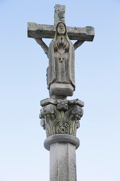 Antiguo crucifijo de piedra blanca con la Virgen María en el cielo azul