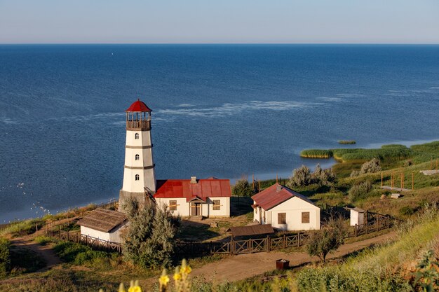 Antiguo faro con techo rojo en la orilla del mar por la mañana.