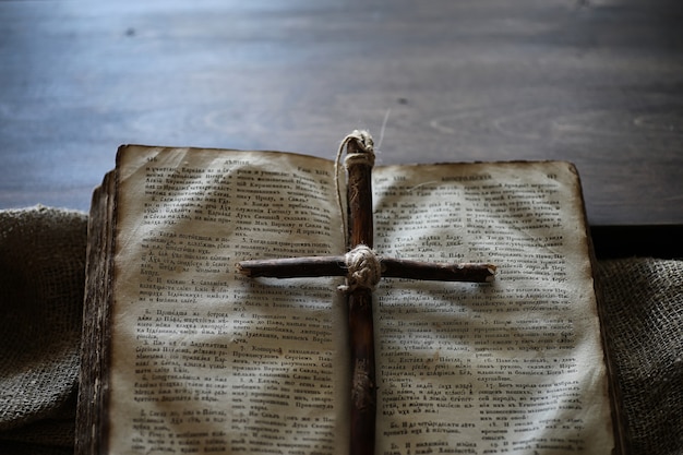 Antiguo libro religioso y cruz de madera en el fondo de madera y arpillera