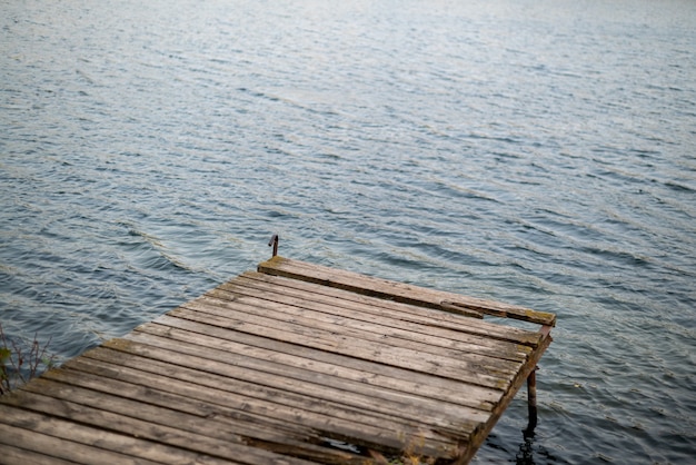 Antiguo muelle de madera con tablas dañadas sobre la superficie del lago ondulado