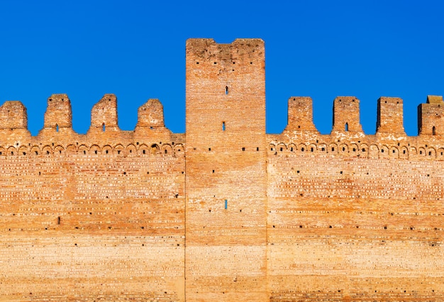 Antiguo muro de ladrillo de la fortaleza medieval italiana contra el cielo azul