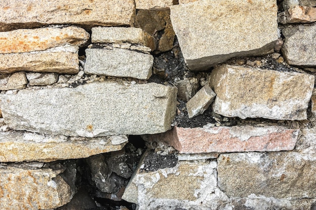 Un antiguo muro de piedra hecho de bloques de granito está siendo destruido por la vejez La textura de la piedra