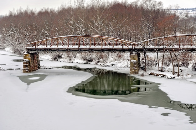 Antiguo puente de carretera de acero sobre el río después de las nevadas