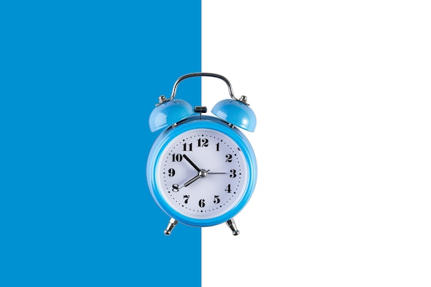 Antiguo reloj de alarma azul en la pared azul y blanca. Reloj vintage plano creativo en la pared de color, espacio de copia en estilo minimalista, plantilla vacía para texto