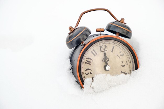 Antiguo reloj de alarma retro en invierno en la nieve sobre fondo blanco muestra doce horas.