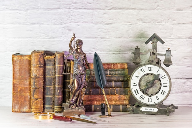 Antike Uhr zusammen mit antiken Büchern und Statuette der Göttin der Gerechtigkeit. temis.