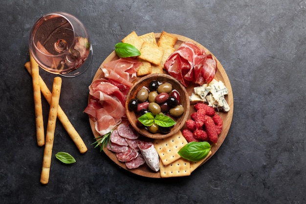 Antipasti-Brett mit Prosciutto-Salami-Crackern, Käse, Nüssen, Oliven und Roséwein Draufsicht flach liegend