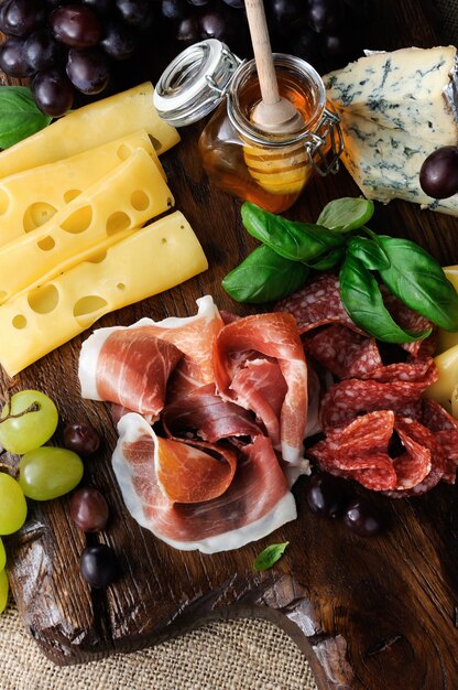 Antipasti-Catering-Platte mit Speck-Prosciutto-Salami-Käse und Trauben auf Holzuntergrund