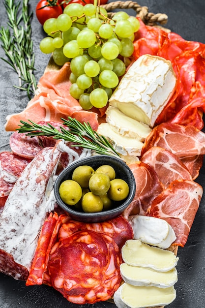 Antipasti-platte kaltes fleisch mit trauben, schinken, schinkenscheiben, trockenfleisch vom rind, chorizo-salami, fuet, camembert und ziegenkäse. schwarzer hintergrund. draufsicht