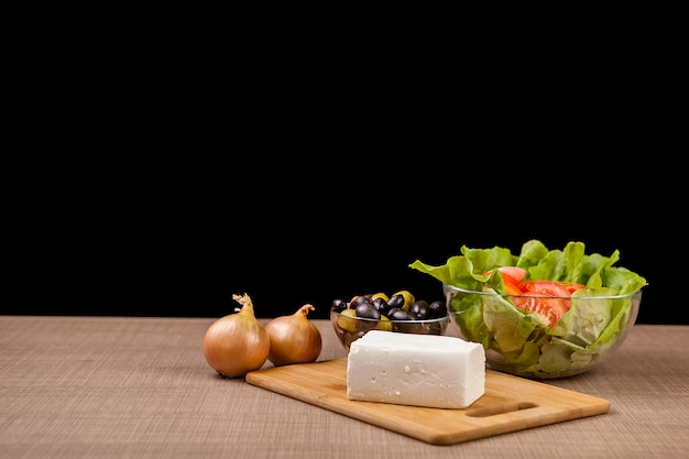 Antipasto fresco de queso feta, cebollas y dos tazones de vidrio con ensalada fresca y aceitunas sobre fondo negro