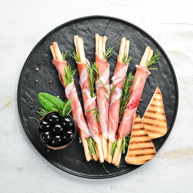 Antipasto italiano Palitos de pan grissini con jamón prosciutto en un plato negro Estilo rústico Vista superior Espacio libre para el texto