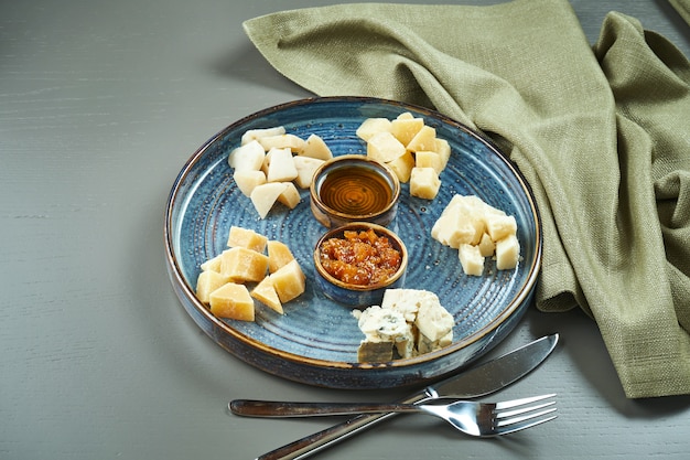 Antipasto - un plato de queso. Diferentes quesos caseros en un plato de cerámica: brie, camembert, holandés con miel y nueces. Aperitivo de vino.