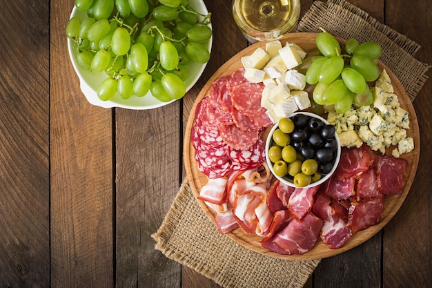 Antipasto prato de catering com bacon, queijo salame e uvas em um fundo de madeira