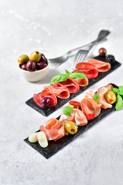 Foto antipasto en restaurante italiano con jamón y salami, aceitunas. servido en platos de piedra negra.