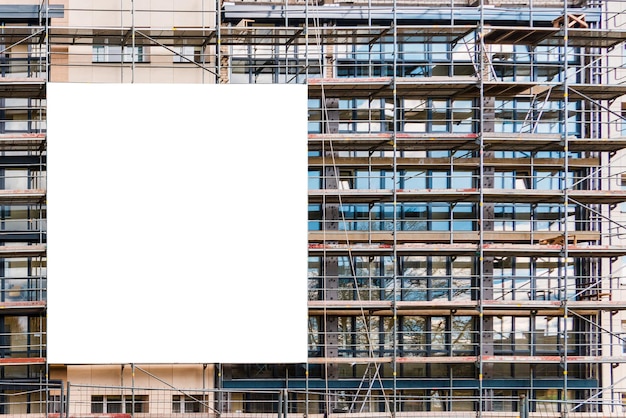 Anuncio blanco en blanco colgado en el andamio de un edificio moderno en construcciónReconstrucción de un edificio con cartel blanco