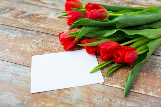 anuncio, día de san valentín, concepto de saludo y vacaciones - cierre de tulipanes rojos y papel en blanco o carta sobre fondo de madera