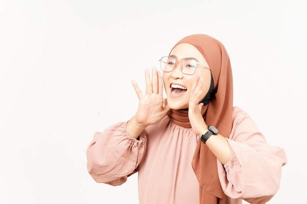Anuncio con las manos sobre la boca de una hermosa mujer asiática usando hiyab aislado en blanco