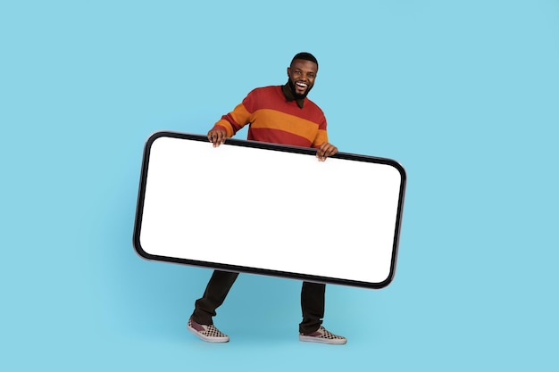Anúncio móvel feliz jovem negro carregando grande smartphone em branco