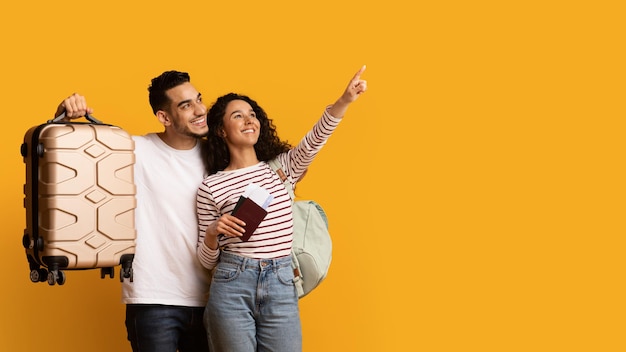 Foto anuncio de viaje pareja árabe alegre con maleta y pasaportes apuntando hacia afuera