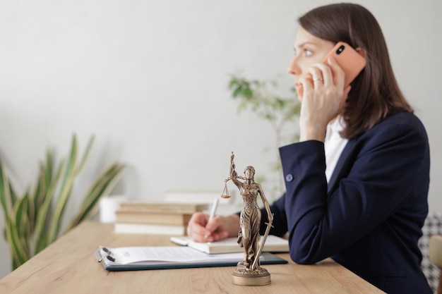 Anwältin in einer leichten Jacke arbeitet in einem Büro eine Statuette von Themis, der Göttin der Gerechtigkeit