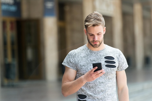 Anwendung herunterladen Man hält Smartphone Gebäude Hintergrund Man Messaging Online Smartphone Moderne Smartphone-Anwendung Einfache Kommunikation E-Mail senden Antwortnachricht Städtische WLAN-Abdeckung