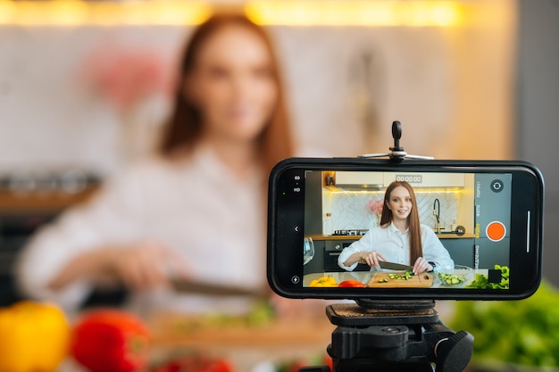 Anzeige des Video-Blogs mit Kameraaufnahme für Food-Blogger-Frau, die Gemüse in der modernen Küche schneidet