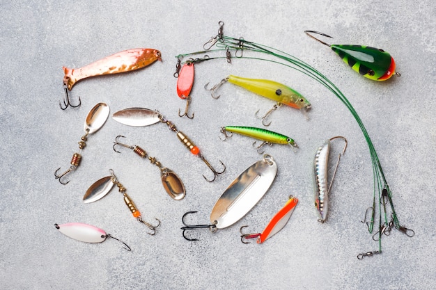 Anzuelos y cebos en un conjunto para la captura de diferentes peces en una mesa gris con espacio de copia. Lay Flat