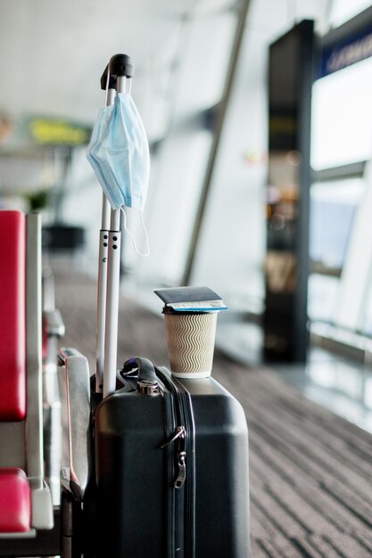 Ao lado dos assentos em um aeroporto vazio está uma mala em que está um copo de café