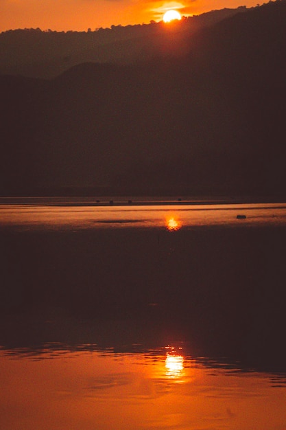 Ao pôr do sol, paisagem montanhosa da silhueta do lago reflexão Sol se pondo atrás das montanhas