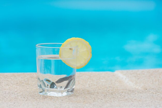 Foto apagar a sede no verão para vencer o calor um copo de água com uma fatia de limão na borda de uma piscina