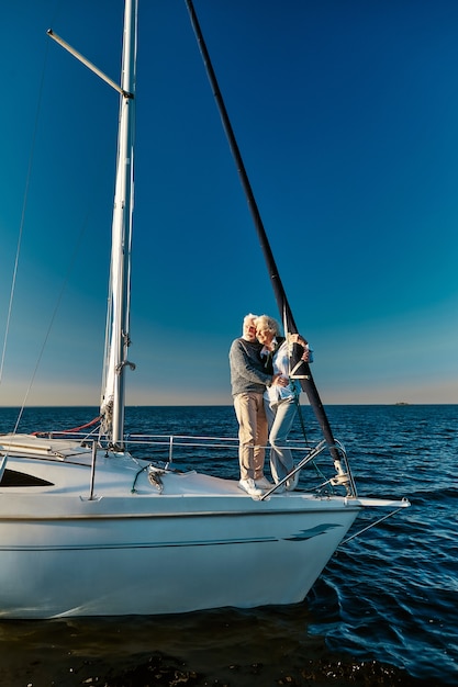 Apaixonado pelo mar em todo o comprimento de um lindo casal de idosos em pé ao lado de um barco a vela ou