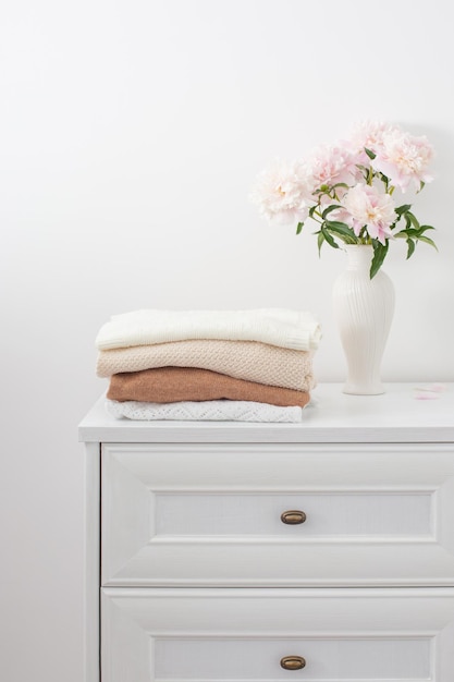 Aparador blanco con ropa y flores en la habitación blanca.