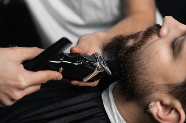 Aparar a barba com uma máquina de barbear. Publicidade para barbearia e salão de beleza masculino.